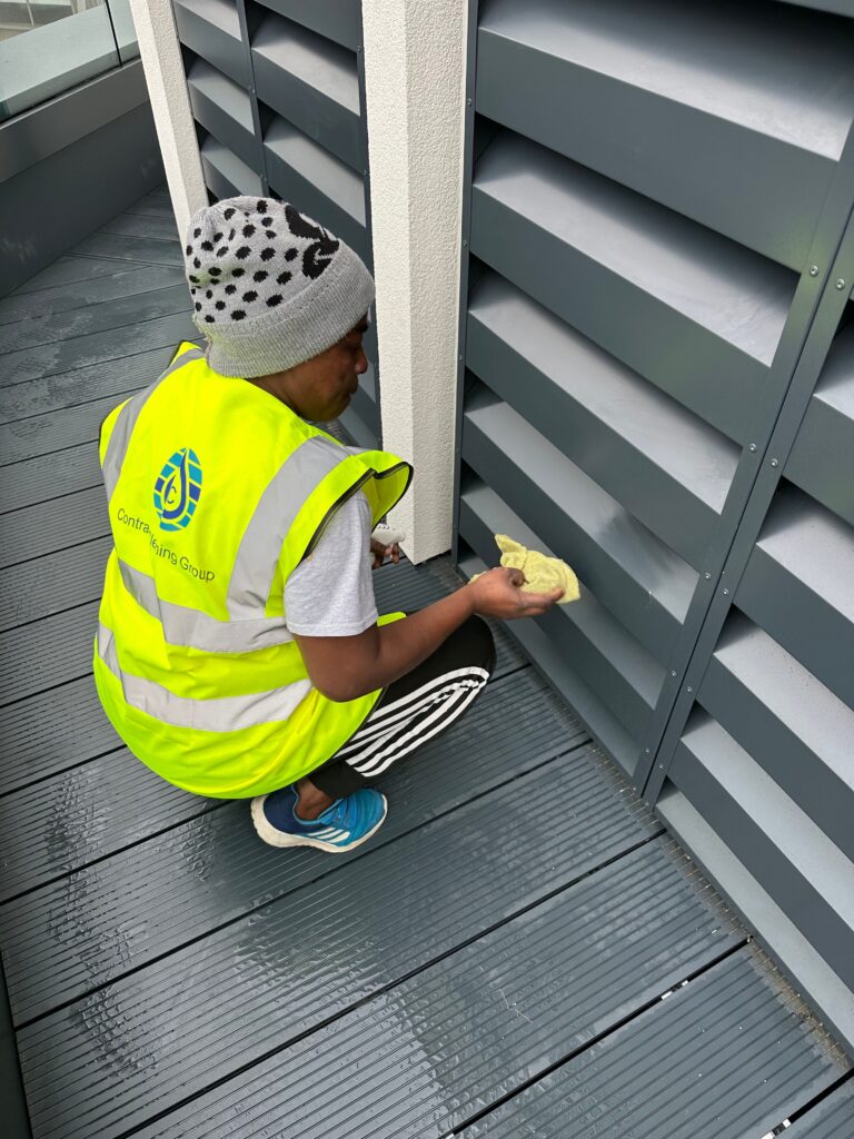 Cleaner from Contract Cleaning Group wearing a high-visibility vest using eco-friendly cleaning products on external louvres during office cleaning in Hertfordshire, Essex & London